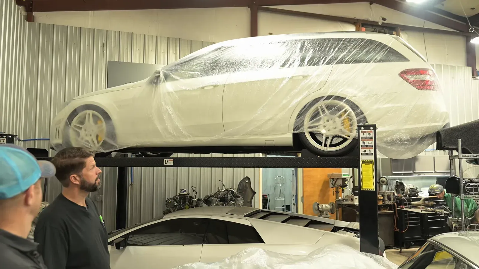 A white Mercedes E63 wagon with white wheels, covered in plastic on a lift at DC MotorWerks