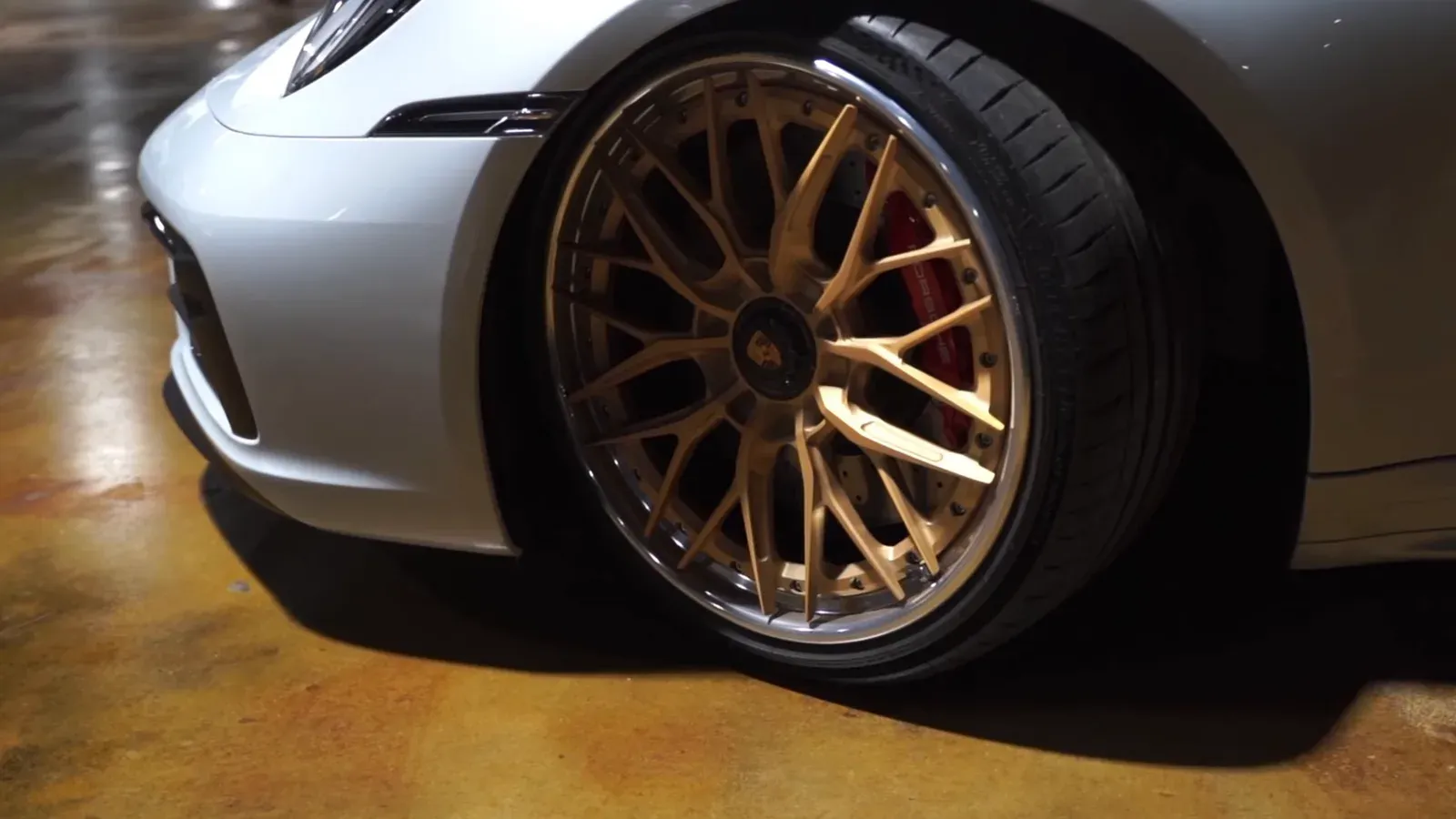 A gold multi-spoke wheel and red brake caliper on Dani Butler’s Ice Gray Metallic Porsche 992.1 GTS