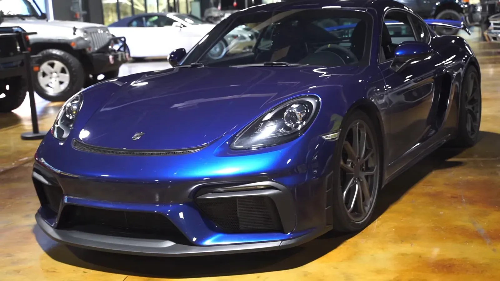 A blue Porsche 718 GT4 parked on the lounge floor, seen from the front three-quarter