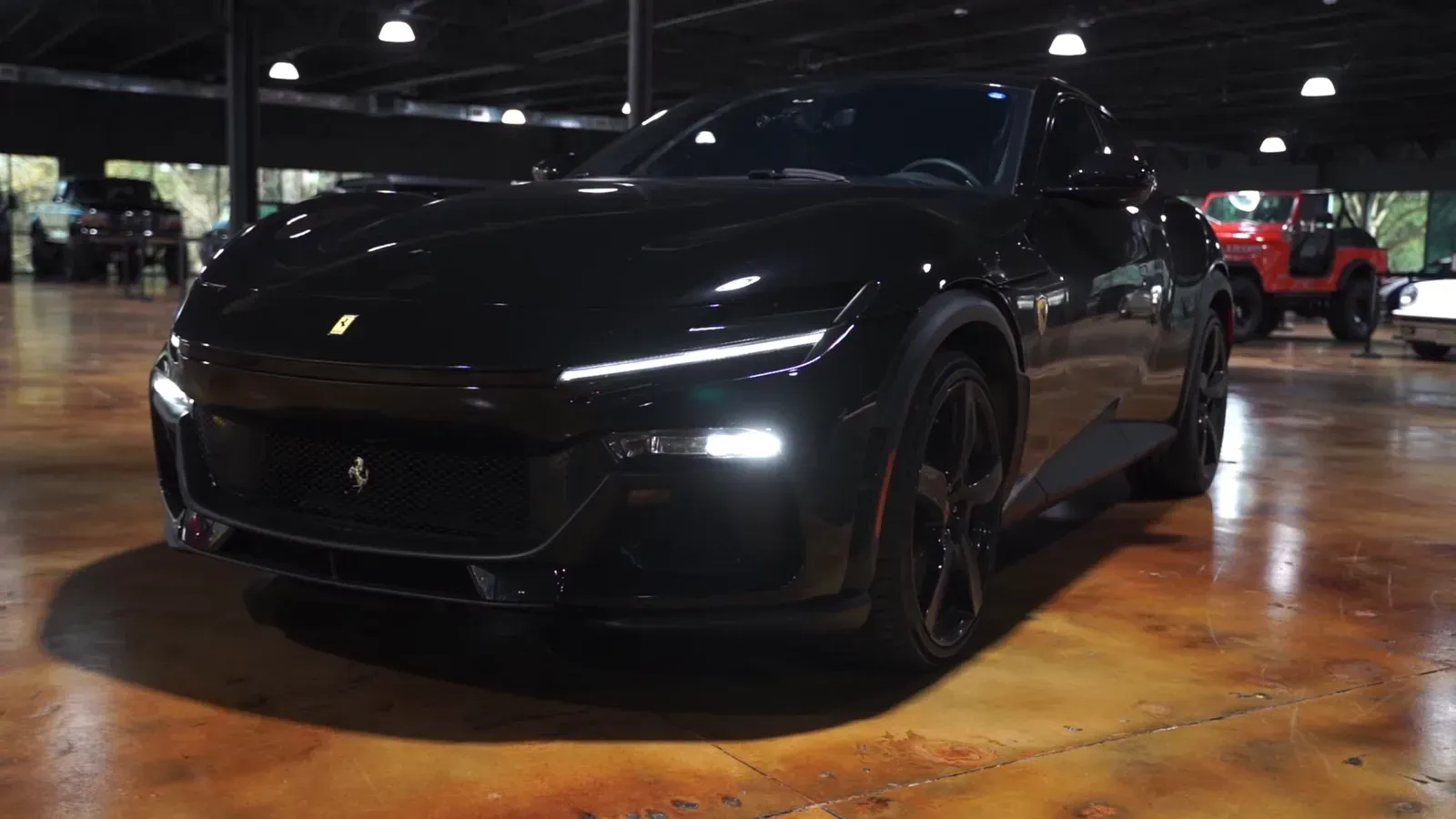 A black Ferrari Purosangue with its daytime running lights on, parked on the lounge floor