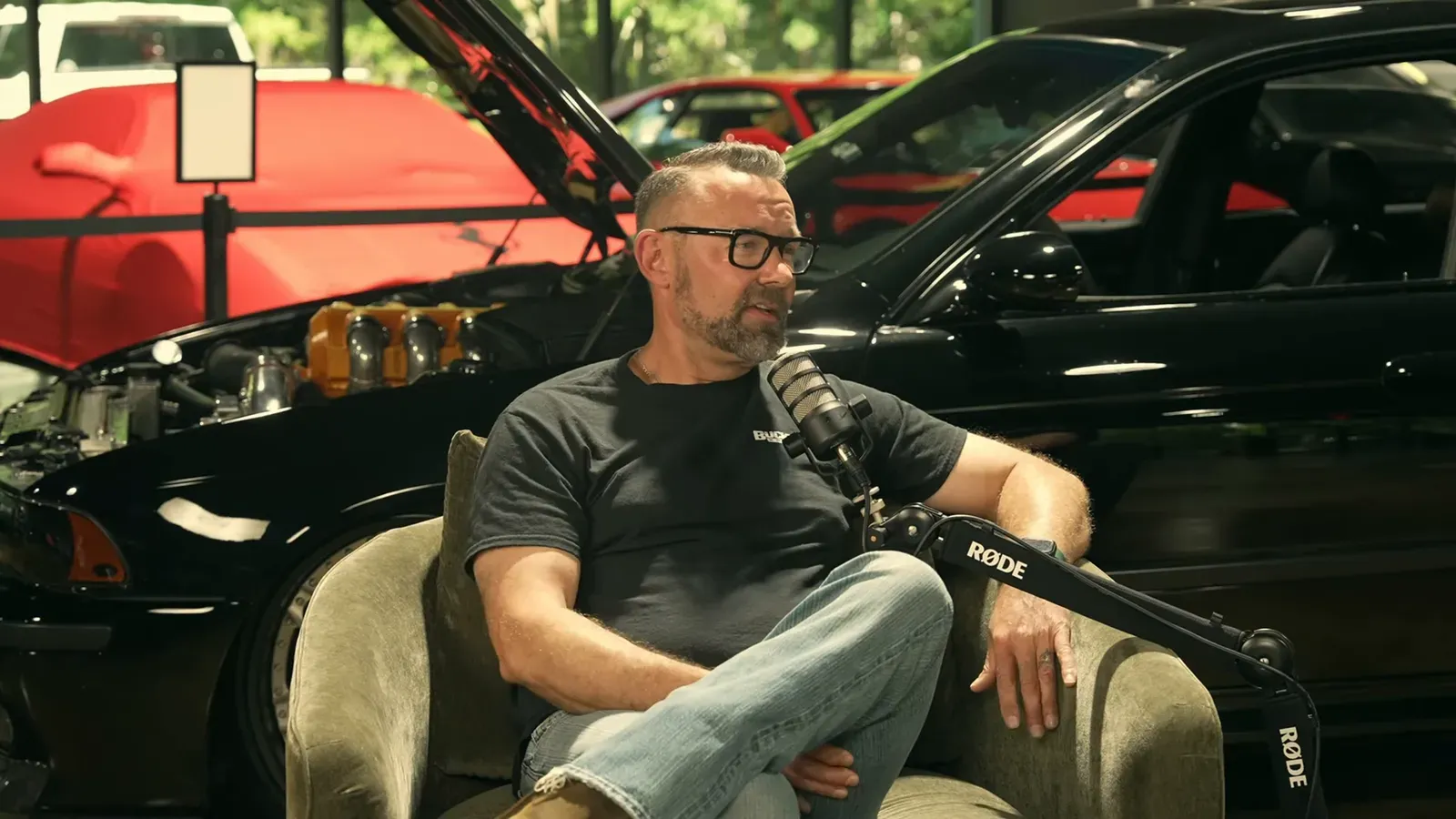 Jason Cummins talking on the Throttlecast set at The Ride Lounge, cars on the floor behind