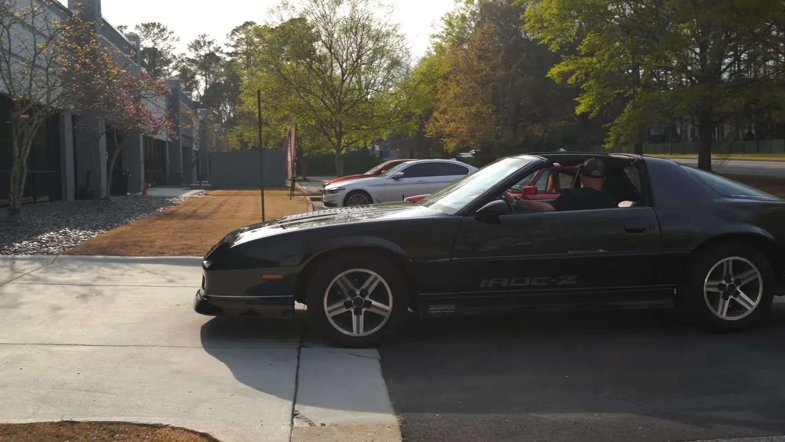 Jim Florek’s black 1987 Camaro IROC-Z driving across a parking lot, side view, a driver at the wheel