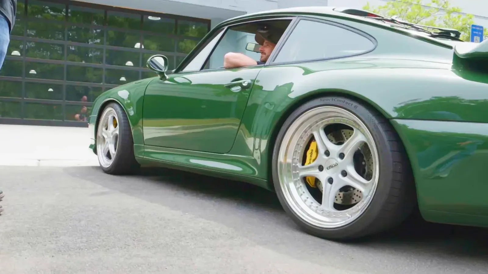 Matt Kossoff’s Irish Green Porsche 993 Turbo rolling past a garage door, side view, a driver at the wheel