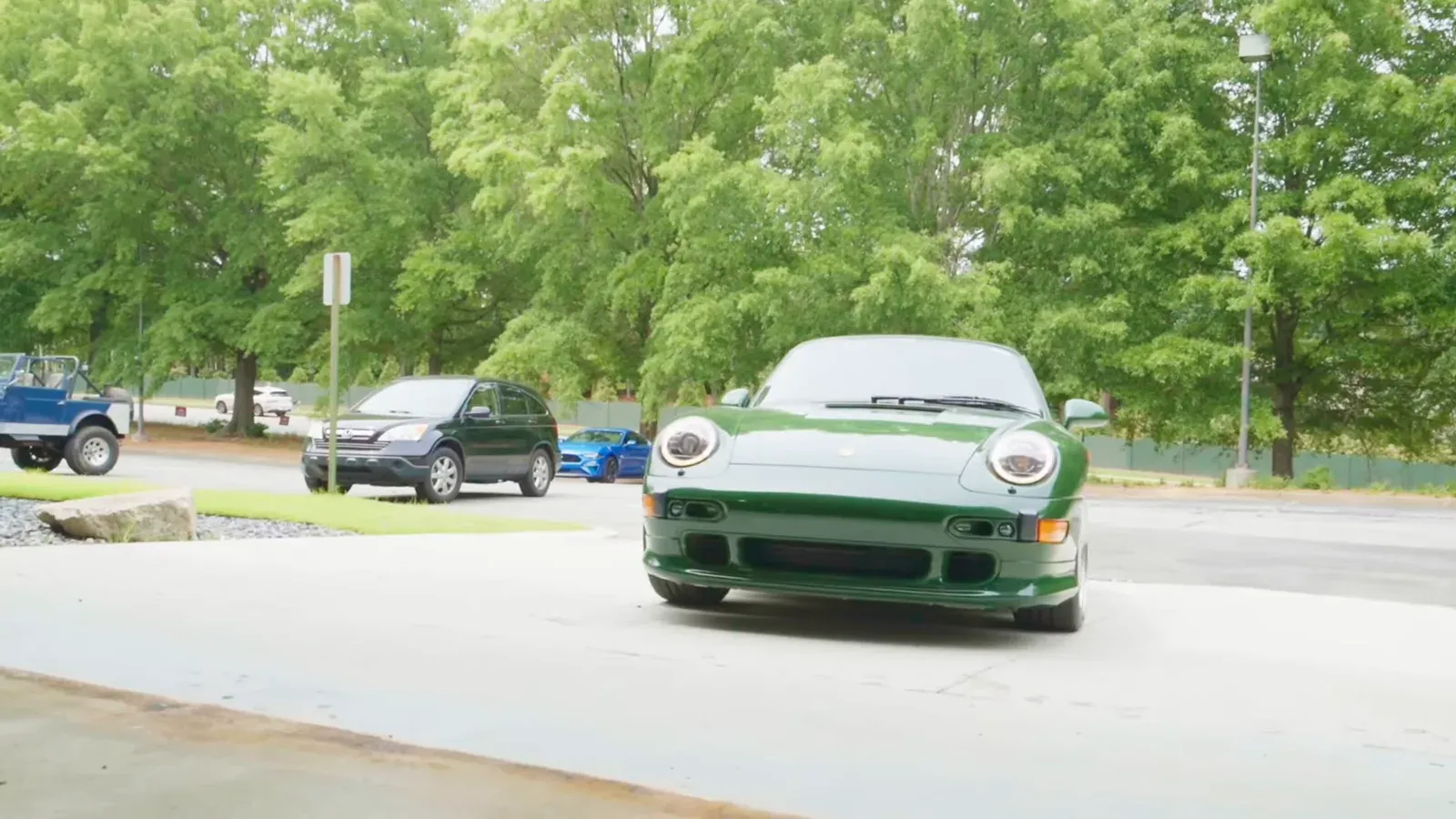 Front of Matt Kossoff’s Irish Green Porsche 993 Turbo pulling into a parking lot, trees behind