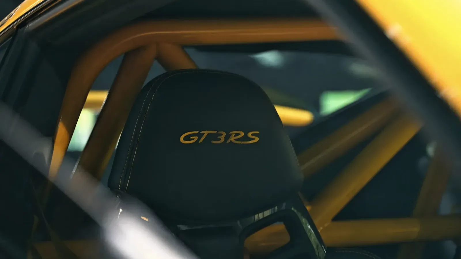 A carbon bucket seat embroidered GT3 RS inside Parker Smith’s Porsche, framed by a yellow roll cage