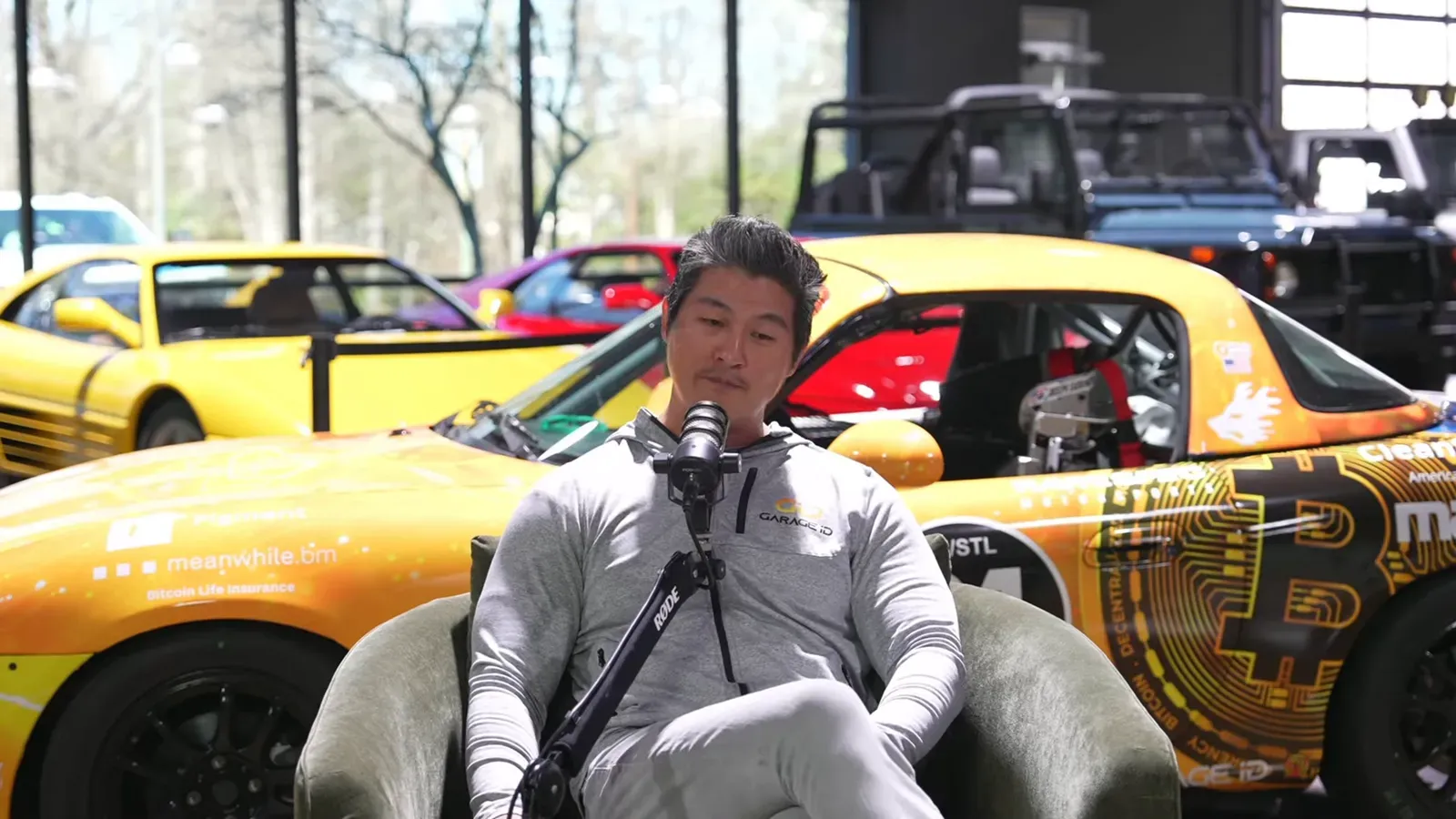 Peter Saddington talking on the Throttlecast set at The Ride Lounge, cars on the floor behind