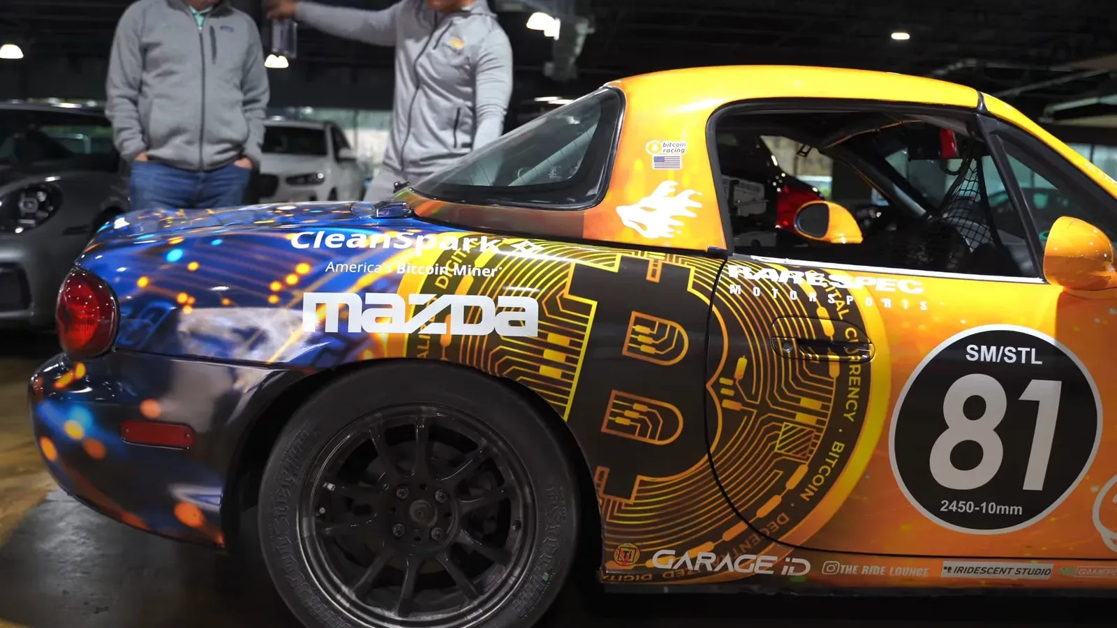 Side view of the Spec Miata in a yellow and blue Bitcoin livery with a roll cage visible through the window