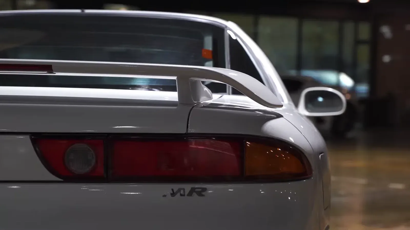 The rear wing and tail light of the white Mitsubishi GTO with an MR badge on the rear panel