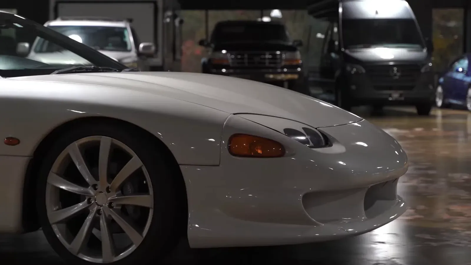 The front corner of the white Mitsubishi GTO MR, its pop-up headlight and front wheel, on the lounge floor