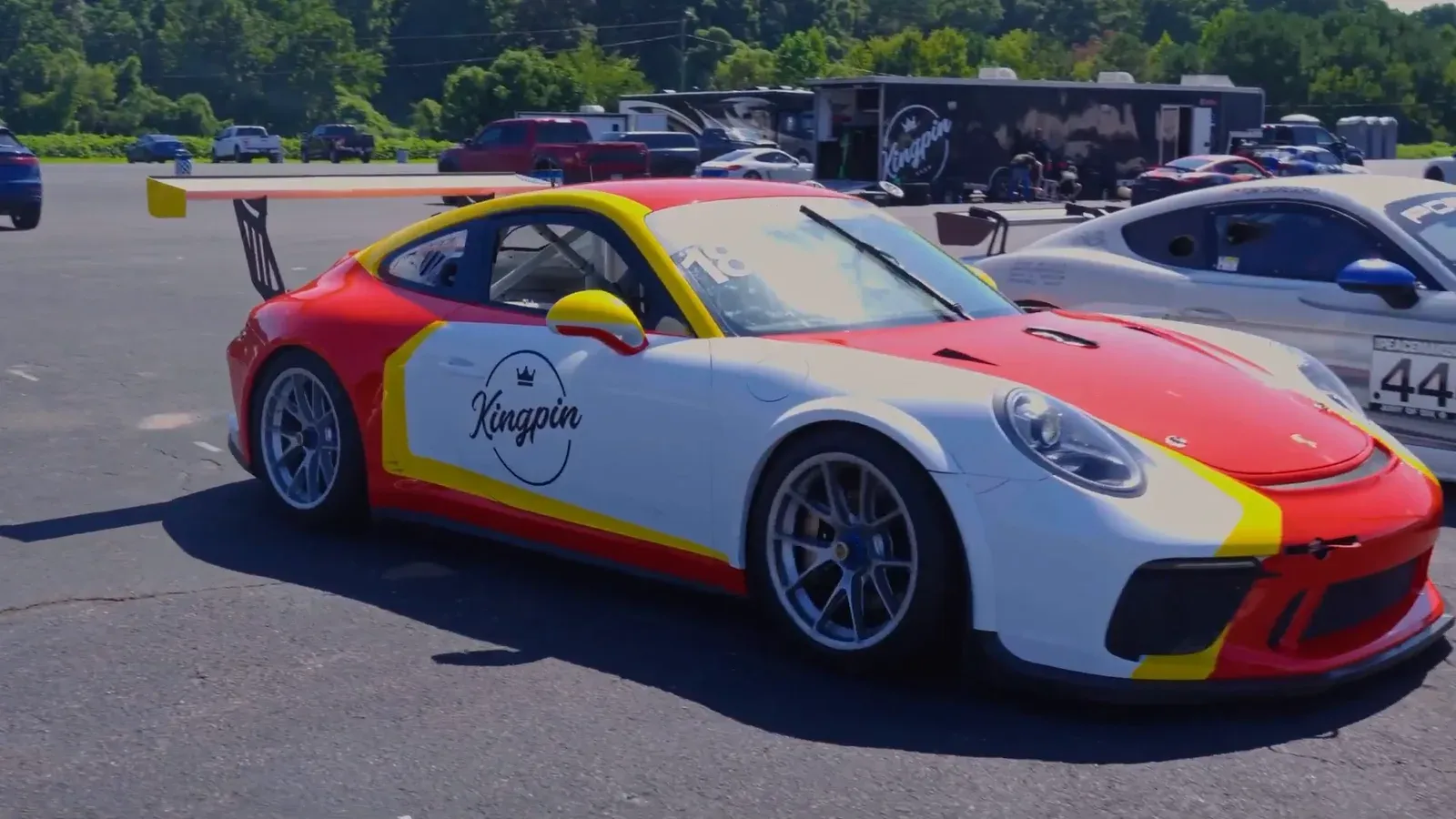 A red, yellow and white Porsche 911 Cup car with a rear wing in the Road Atlanta paddock