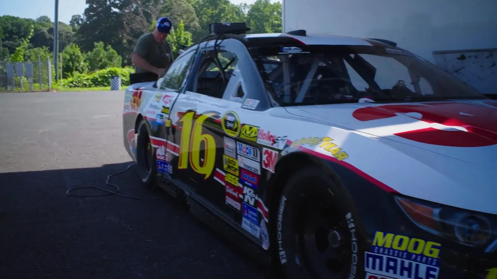 Danny’s white number 16 stock car covered in sponsor decals, parked beside a trailer in the Road Atlanta paddock